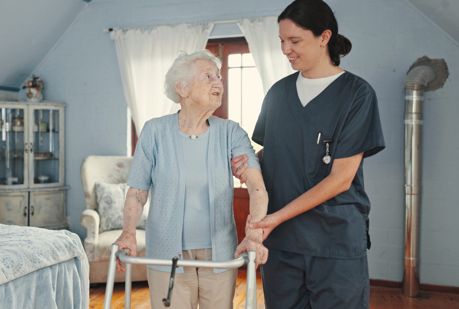 Caregiver assisting an older adult with a walker in a bedroom